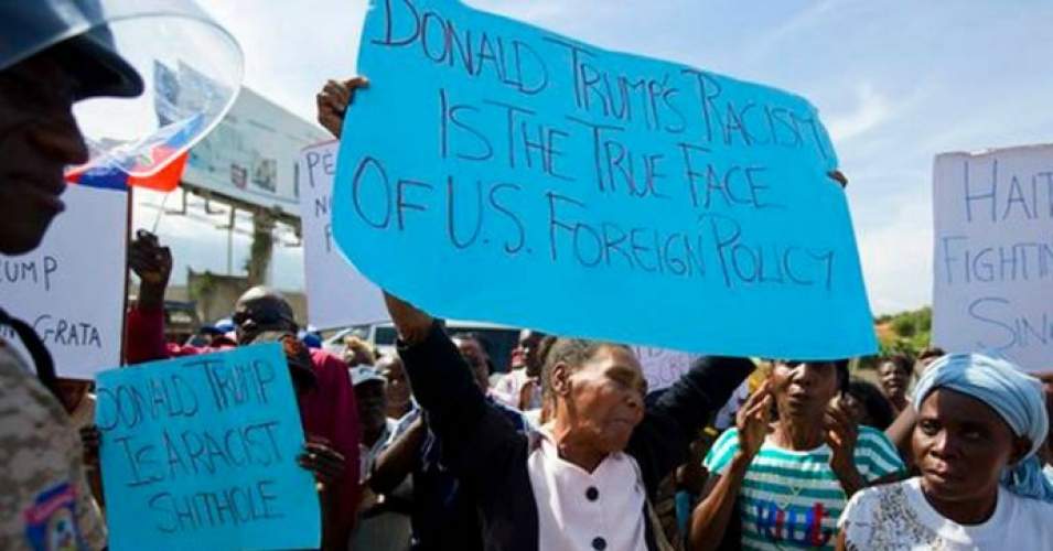 На големия син плакат, който държи жената, пише: „Расизмът на Доналд Тръмп е истинското лице на американската външна политика”. Малкият син плакат гласи: "Доналд Тръмп е расистка лайняна дупка". Снимка: CBS