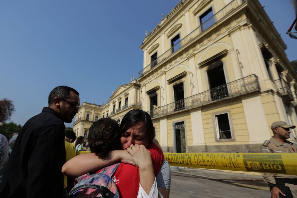 Хората пред изгорелия музей плачат и се прегръщат в опит да се утешат взаимно. Снимка: EFE