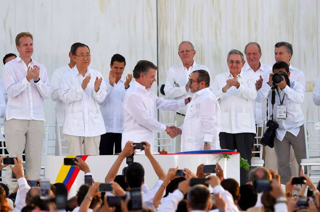 Президентът на Колумбия Мануел Сантос стиска ръката на представителя на ФАРК Родриго Лондоньо-Тимошенко на церемонията в Картахена де Индиас под аплодисментите на високопоставени гости от света