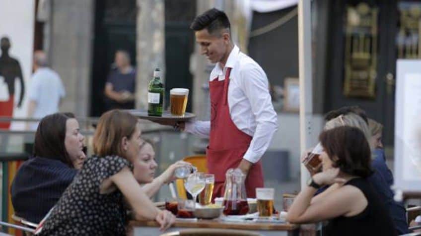 Щастлив от заетостта си келнер обслужва летни туристки на площад "Санта Ана" в Мадрид