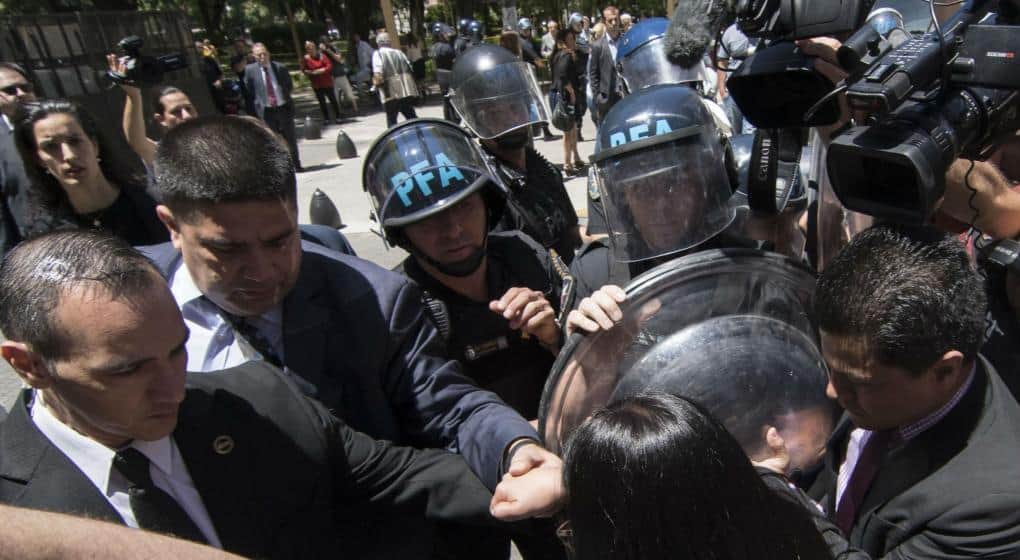 Женската глава в гръб на преден план е на Делси Родригес. Аржентински полицаи я дърпат за ръката.