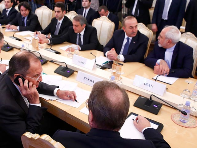 Край масата на тристранните преговори в Москва са Сергей Лавров (с телефона на преден план), както и колегите му от Турция и Иран–Мевлют Чавушоглу и Джават Зариф (срещу него)