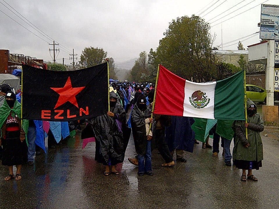 Шествие на сапатистки активисти издига наравно знамето на организацията и националния флаг на Мексико. Снимка: globalproject.info