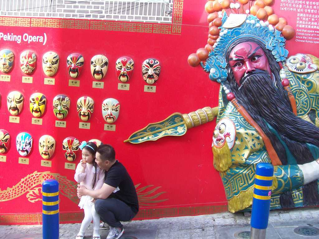 Татко и дъщеричка на фона на колоритна реклама за традиционна Пекинска опера с маски. Снимка: Къдринка Къдренова