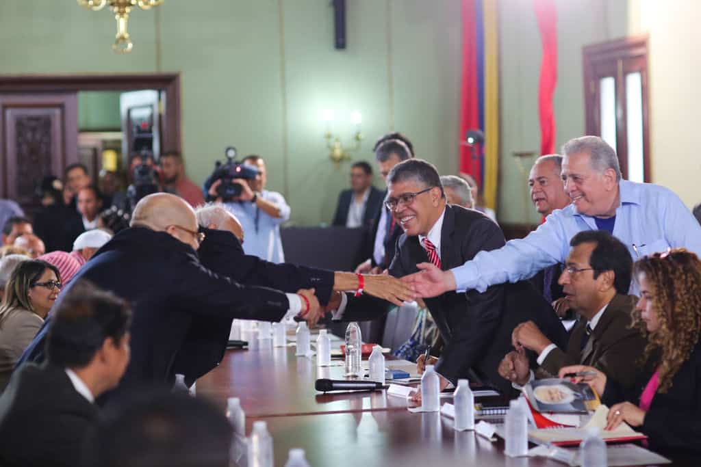 Елиас Хауа (вдясно, наведен през масата за ръкуване, с очила и в костюм) по време на срещата с представители на 17 опозиционни партии с цел установяване на национален диалог. Снимка: resumenlatinoamericano 