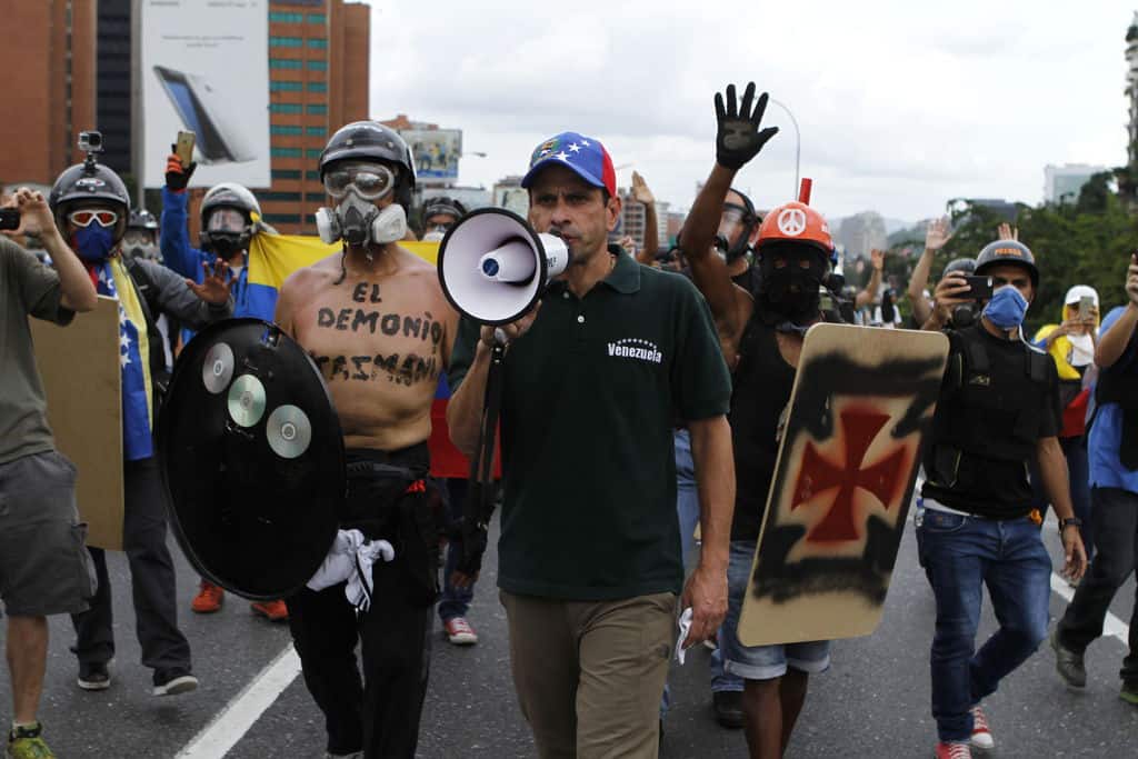 В средата с високоговорителя е опозиционният водач Енрике Каприлес. Отляво негов съратник-протестър се е обозначил върху голия си торс като "Тасманийският дявол". А вдясно почитател явно на тевтонците и на нацистките ордени си е нарисувал символа им върху самоделния щит. Снимка: albaciudad