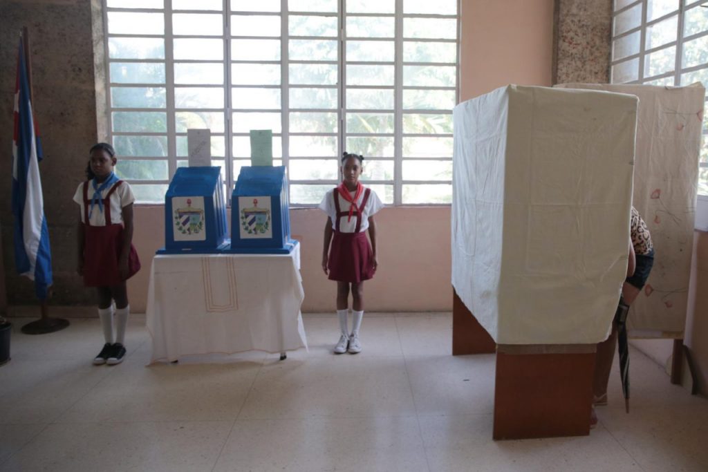 Пионерчета охраняват изборните урни, докато избирател гласува в "тъмната стаичка". Снимка: Resumen Latinoamericano