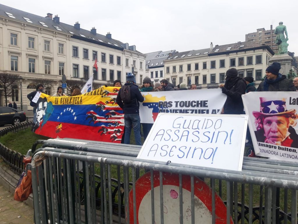 "Гуайдо - убиец", пише на италиански и на испански на преден план. Плакати против намесата на САЩ във Венесуела и в цяла Латинска Америка разпънаха участниците в протеста пред Европейския парламент в Брюксел, където бе подготвено посрещане на венесуелския опозицонер Хуан Гуайдо. Снимка: Ваня Григорова