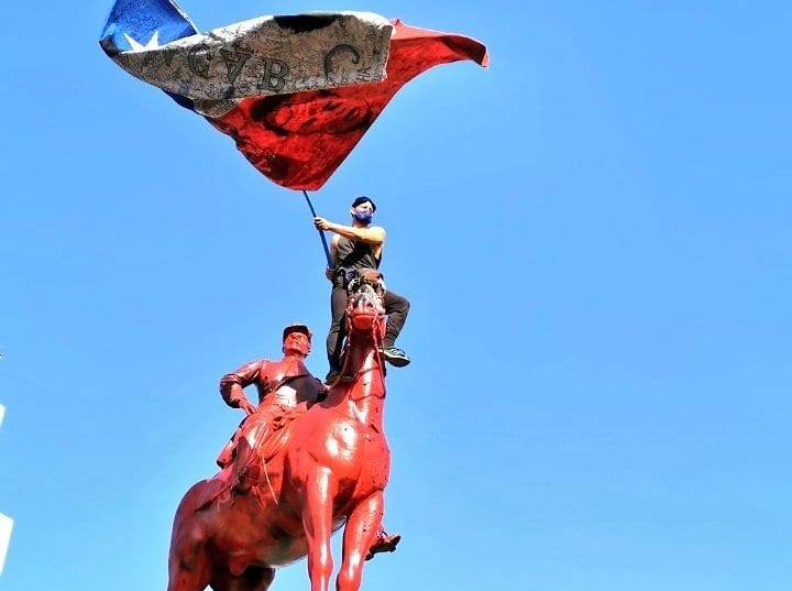 Протестиращ, покачен върху паметника на генерал Бакедано в чилийската столица Сантяго. Снимка: resumenlatinoamericano.org