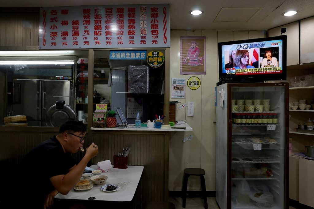 Жител на Тайпе, Тайван, вечеря в заведение, докато по телевизията върви репортаж за посещението на Нанси Пелоси на острова. Снимка: publico.es