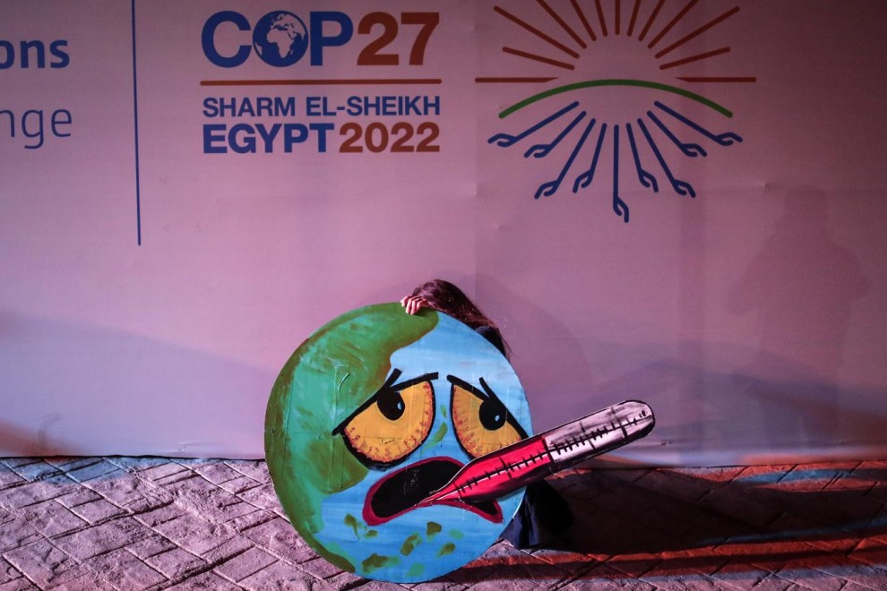 Демонстрантка се е подпряла зад постера си пред стена с логото на климатичната конференция на ООН в Египет COP27. Снимка: EFE