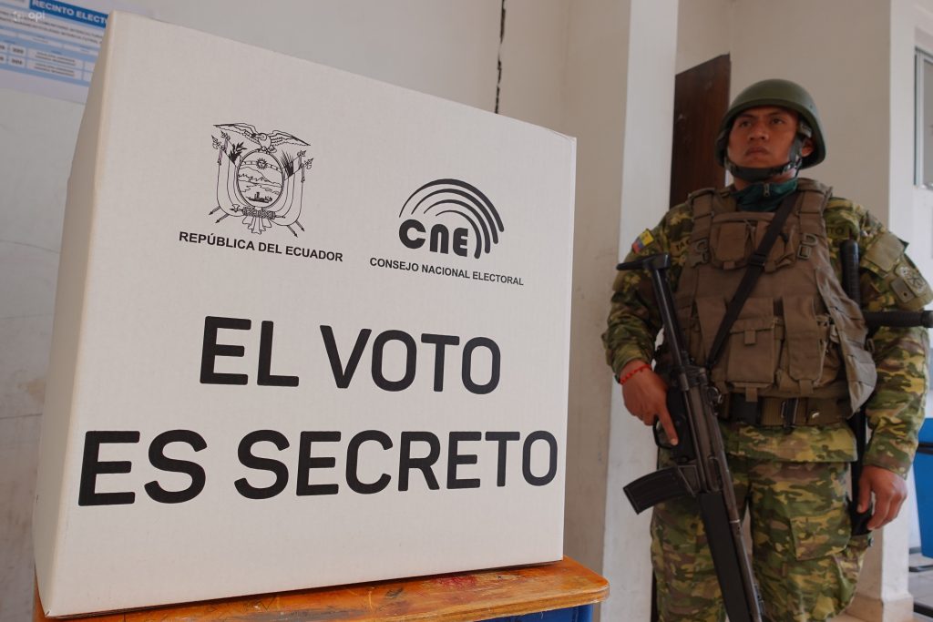 Въоръжен войник бди край един от картонените паравани, зад каквито гласуват еквадорците по секциите си. Снимка: eluniverso.com