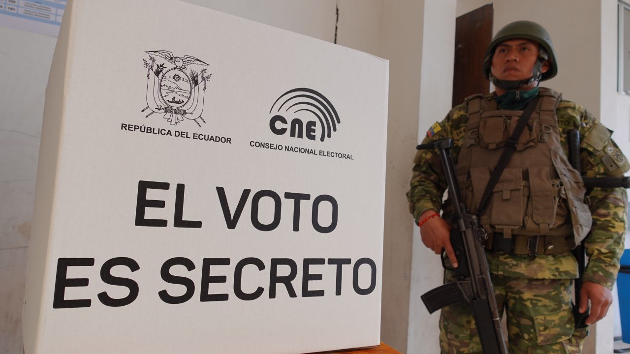 Въоръжен войник бди край един от картонените паравани, зад каквито гласуват еквадорците по секциите си. Снимка: eluniverso.com